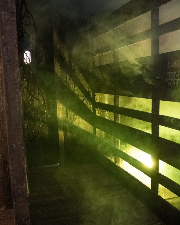Fog and green light streaming through a wooden fence in a dark escape room set
