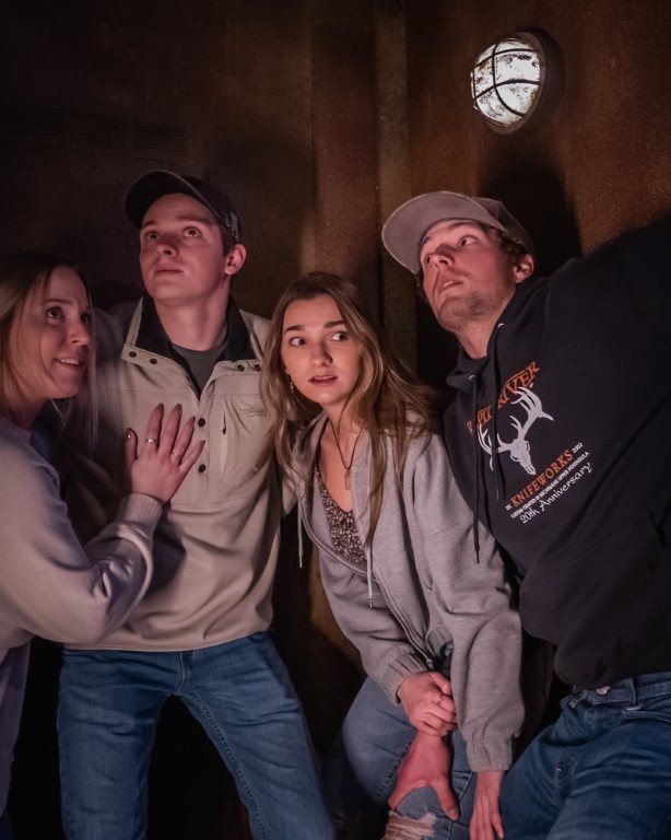 Four players look up nervously in a dark room with rusty walls