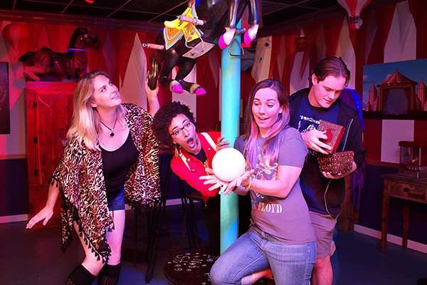 Four players pose with a crystal ball beside a carousel horse in the circus-themed room