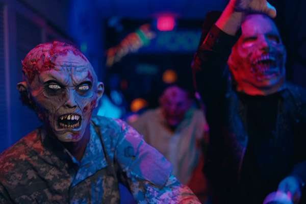 Actors in zombie masks in the neon-lit zombie room