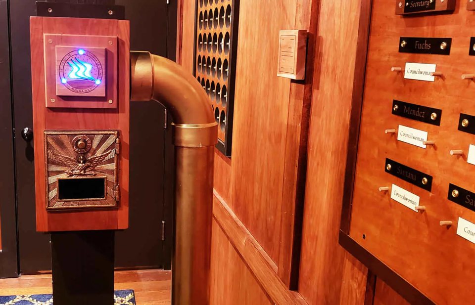 Wood-paneled hall with a glowing mailbox-style prop and a wall of nameplates