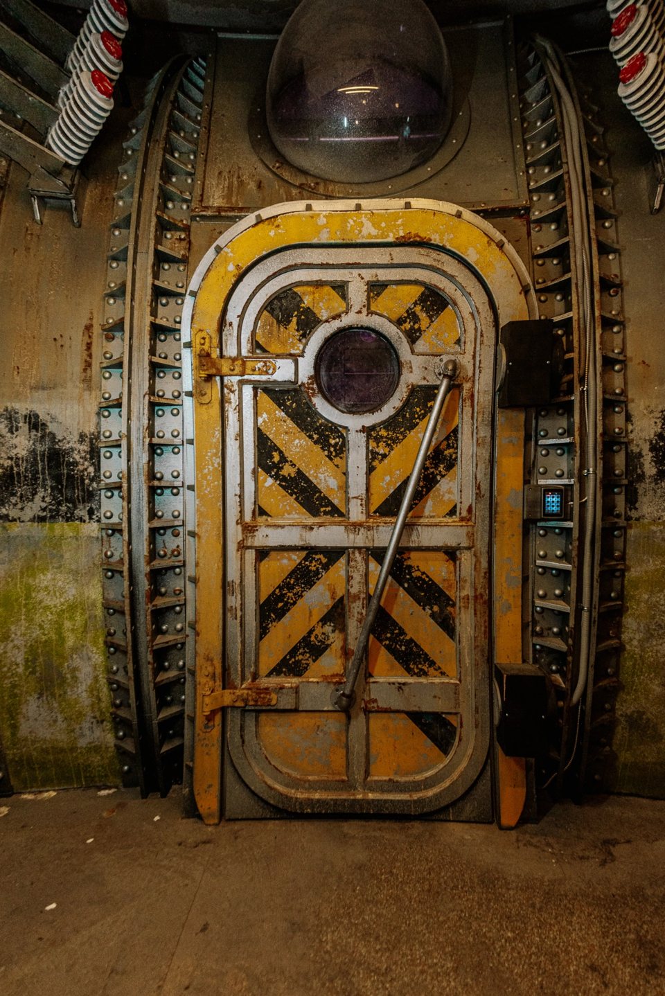 Yellow and black striped riveted steel hatch door with a round porthole