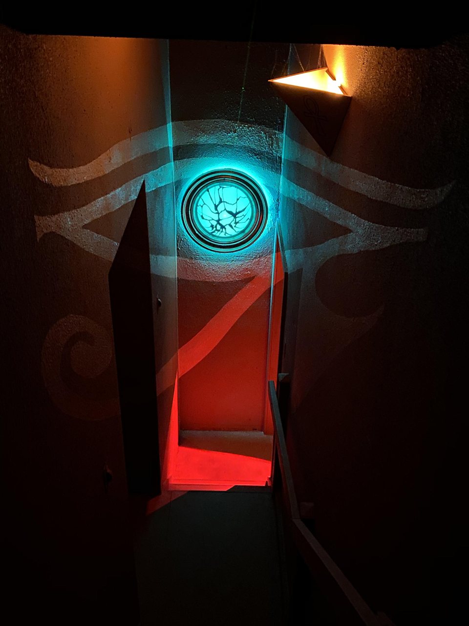 Egyiptomi szemmotívum világító türkiz koronggal egy piros fényű átjáró fölött