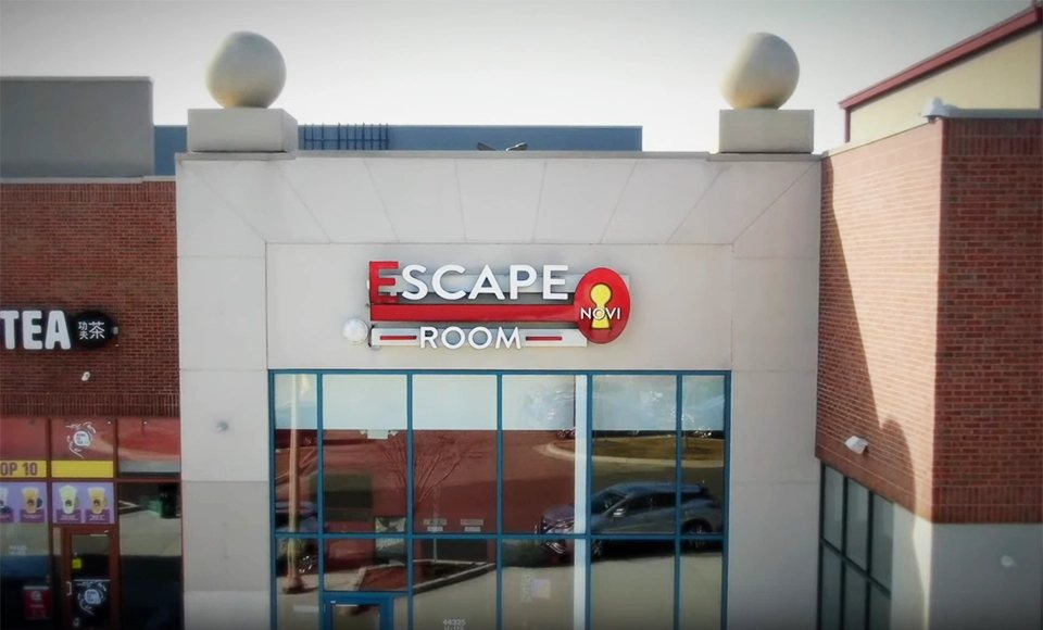 Az Escape Room Novi bejárata piros kulcslyukas cégtáblával egy üzletsoron