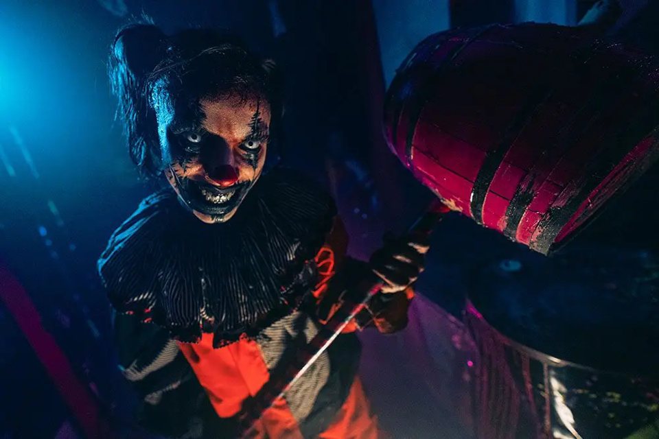 Actor in scary clown makeup holding a giant wooden mallet