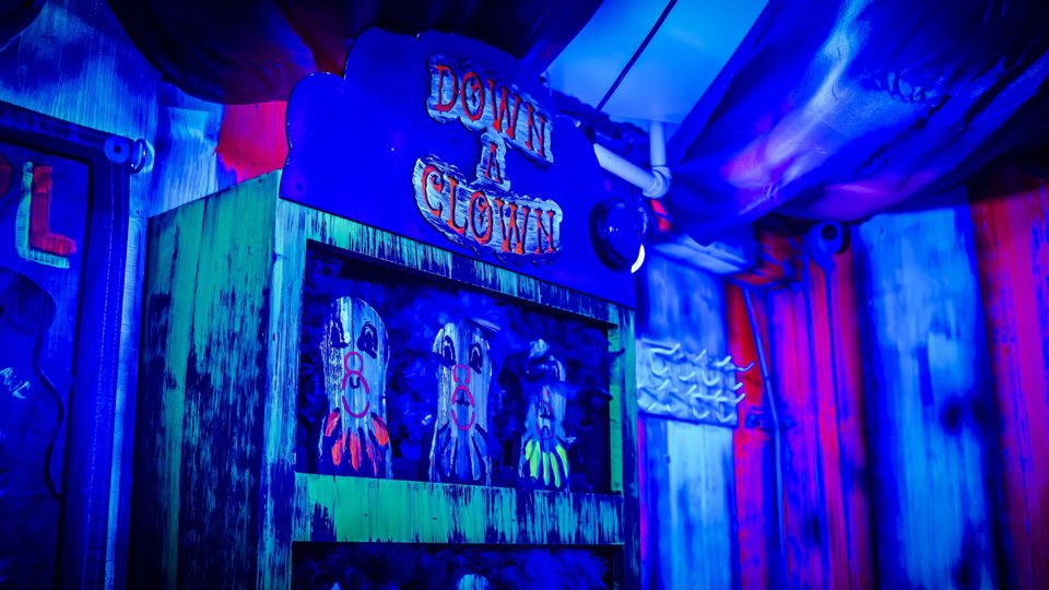Neon-lit Down a Clown carnival game booth in the circus-themed room