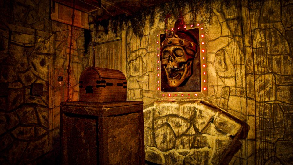 Stone-walled treasure chamber with a wooden chest and a crowned skull relief