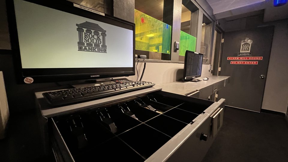 Bank teller counter with a monitor and an open cash drawer in the bank-themed room
