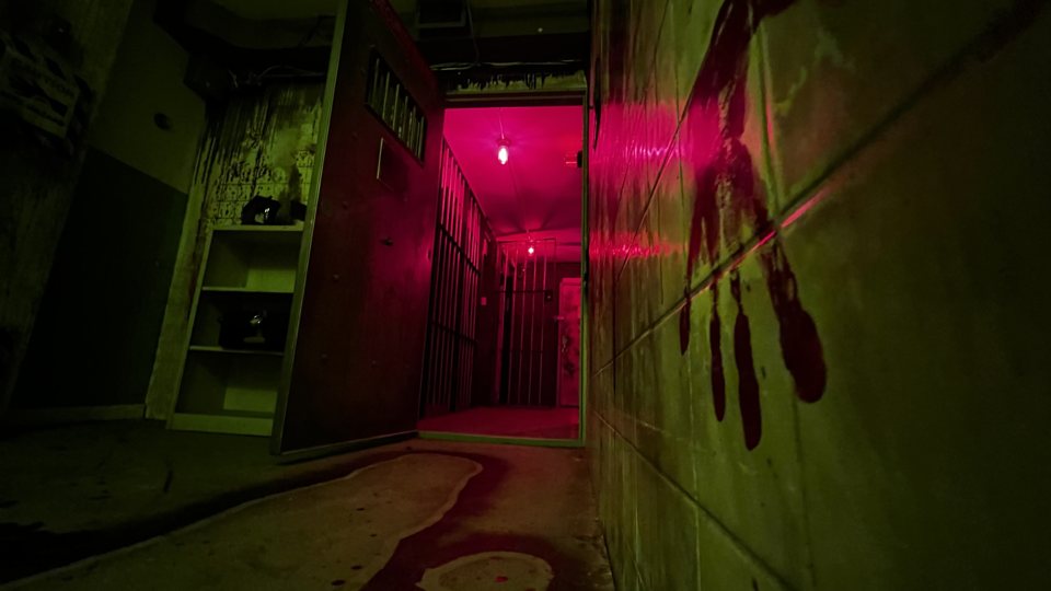 Red-lit prison corridor with a bloody handprint on the wall