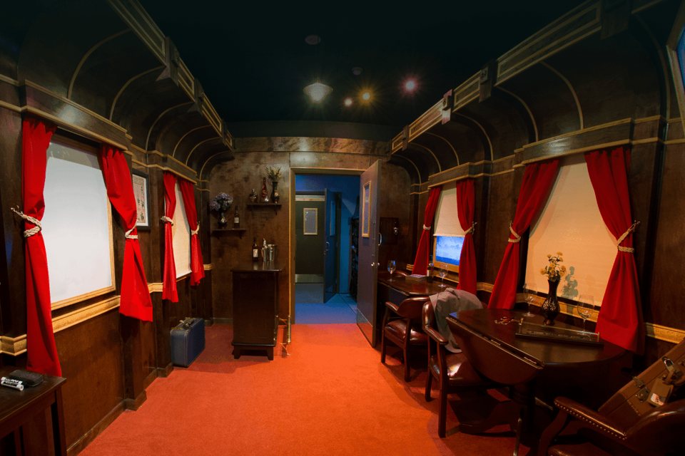 Vintage train car set with red curtains, dark wood paneling, a dining table and leather armchairs