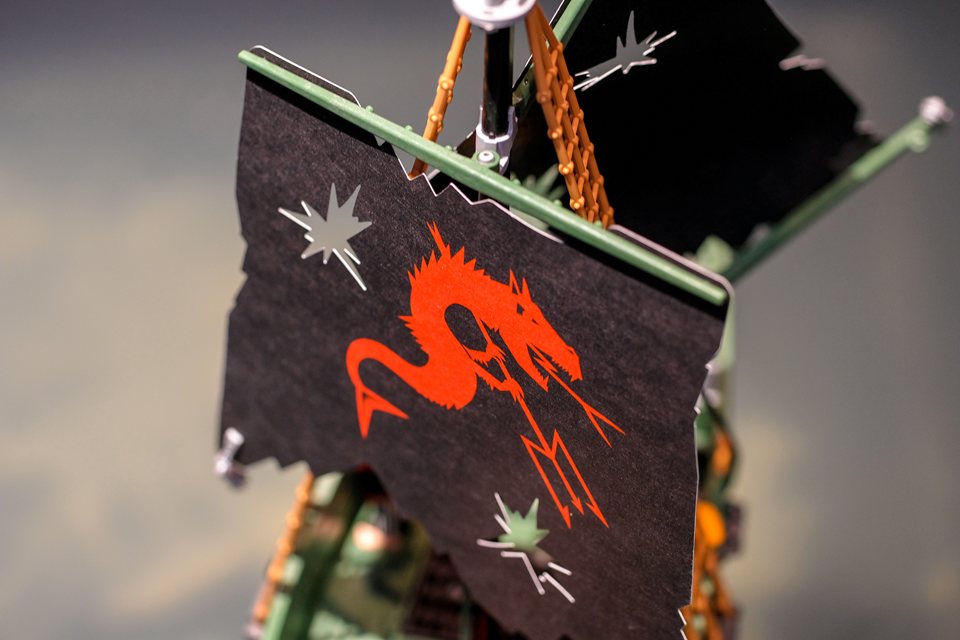 Close-up of a black pirate flag with a red dragon on a model ship's mast