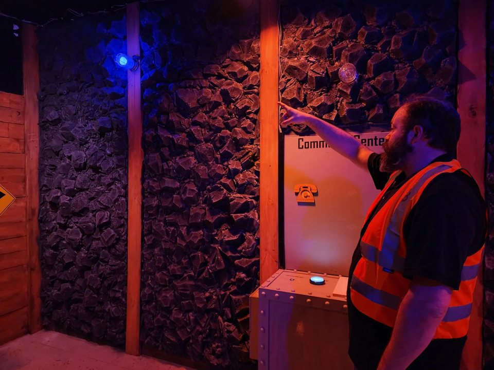 A man in a safety vest pointing at the rock wall in the mine room