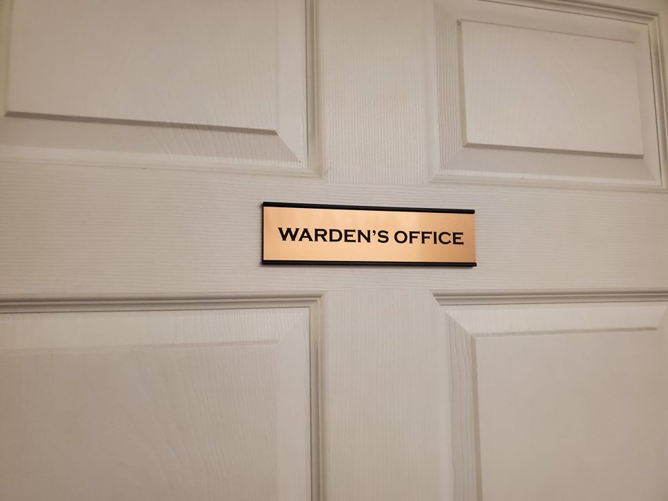 White paneled door with a copper-colored "Warden's Office" nameplate