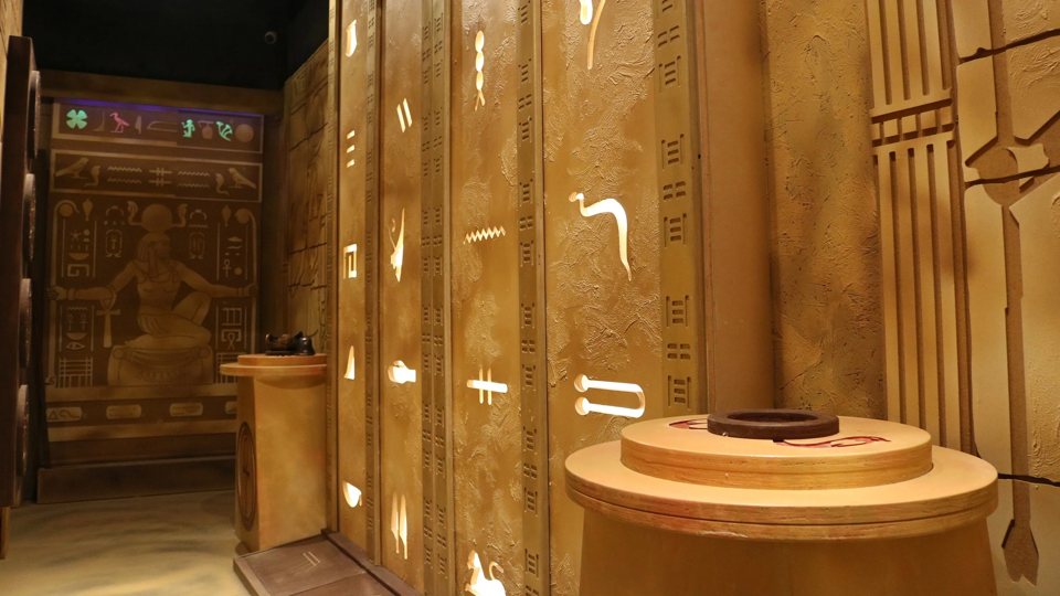 Golden Egyptian tomb set with glowing hieroglyphs, a carved wall relief and round pedestals