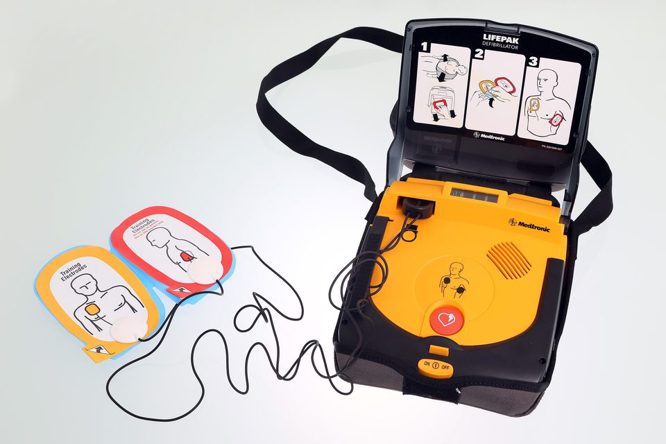 Nyitott AED a két párnával: a fedelén rajz mutatja a lépéseket