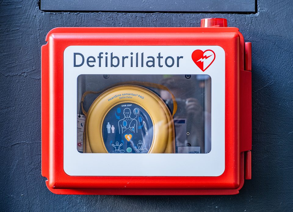 Piros fali szekrény AED-vel, rajta a szív és a „Defibrillator” felirat