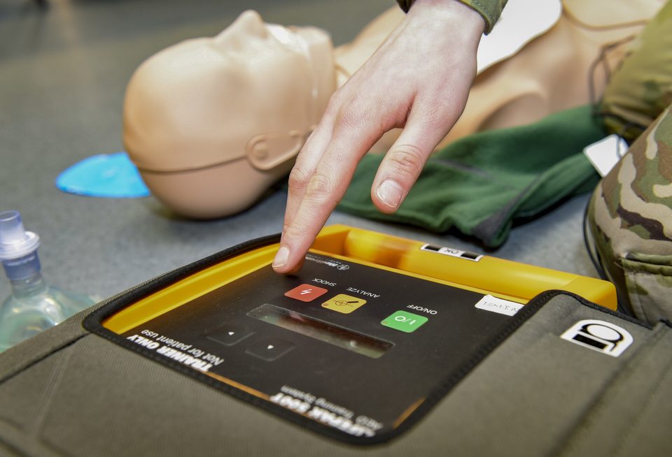 Ujj a sokkgombon egy gyakorló AED-n, mellette újraélesztő baba