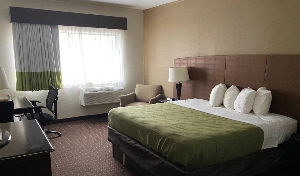 A guest room with a green bedspread, white pillows and a desk