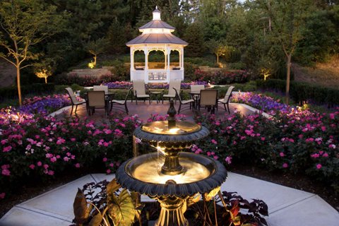The courtyard with a white gazebo, flower beds and a lit fountain in the evening