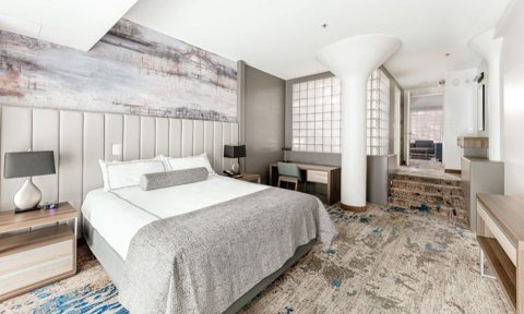 A suite with a king bed, a gray bedspread and a painted wall panel