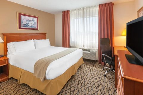 A guest room with a king bed, a desk and a TV
