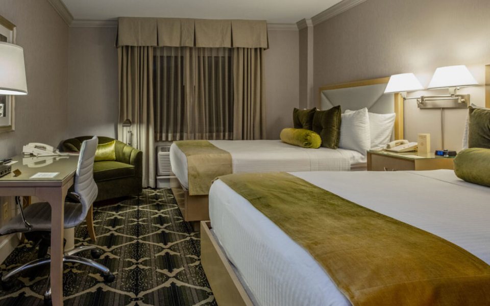 A guest room with two queen beds, green accent pillows and a desk