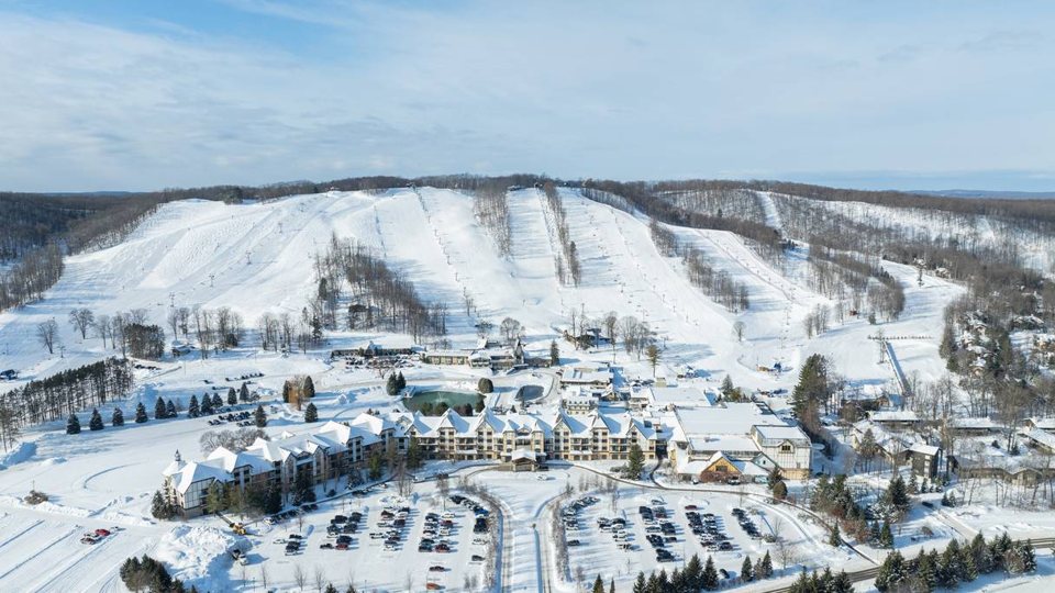 Aerial view of the snowy ski slopes and the resort village at the foot of the hill