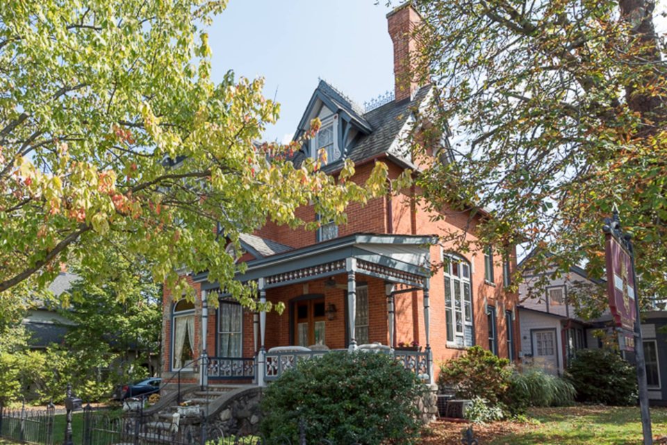 The Victorian brick house with a turreted roof and a porch among the trees