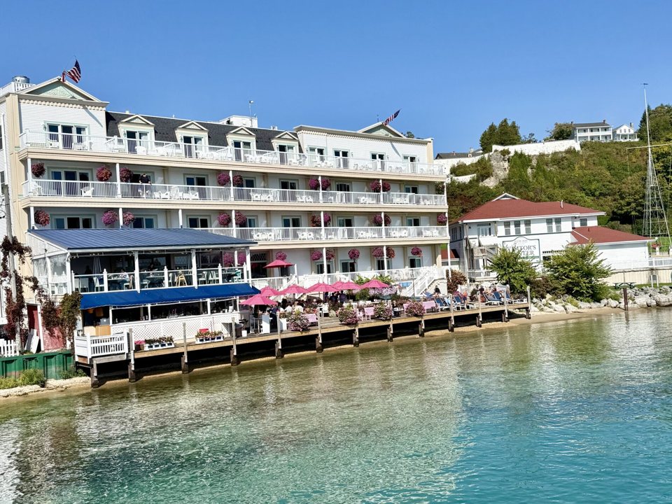 The hotel's white building with balconies on the harbor, with a patio of pink umbrellas