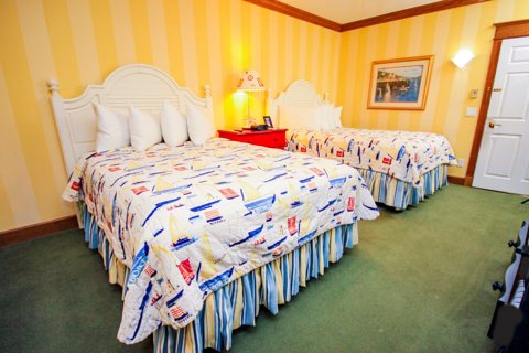 A guest room with two beds, yellow striped wallpaper and sailboat-print bedspreads