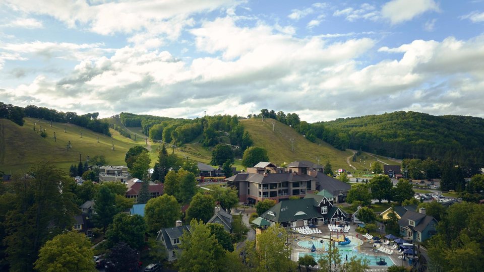 The resort village lodges and pool at the foot of green summer hills