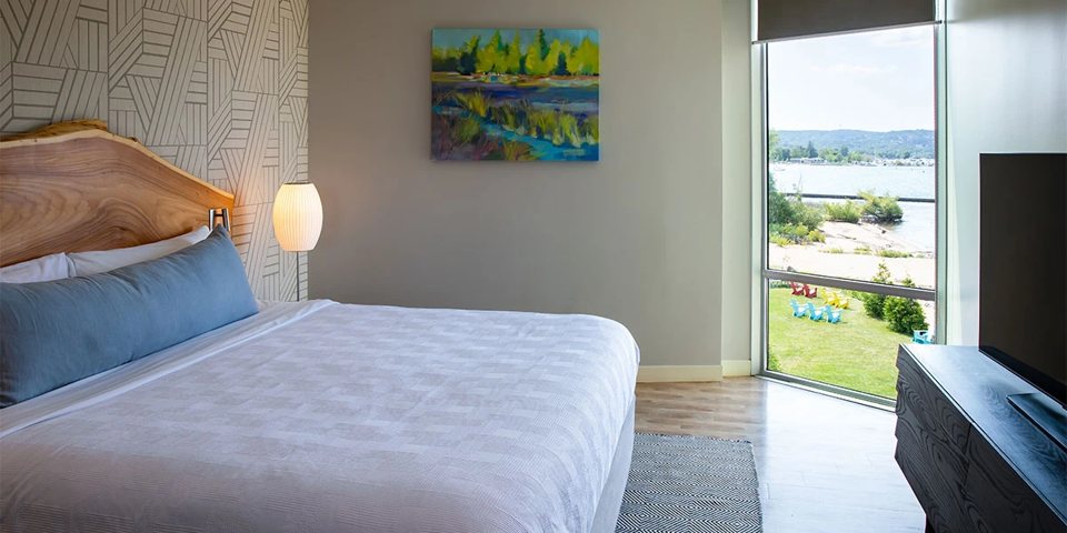 A guest room with a large bed and a floor-to-ceiling window looking out over the lawn and the bay