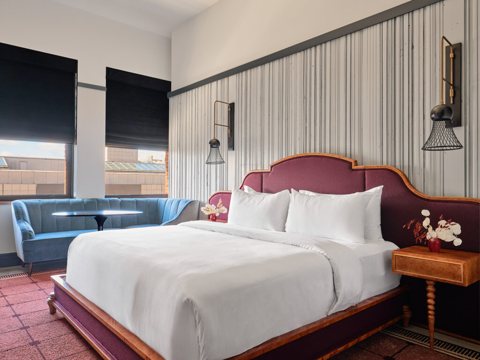 A guest room with a burgundy upholstered headboard, a blue sofa and tall windows