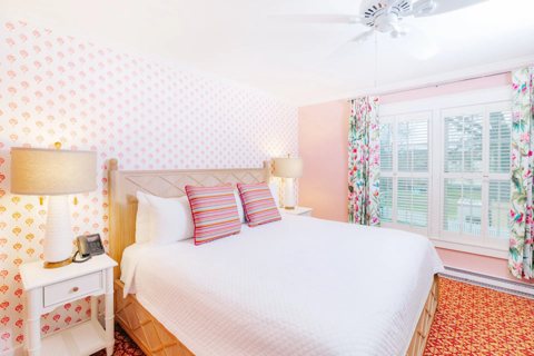 A guest room with pink patterned wallpaper, a large bed and a shuttered window