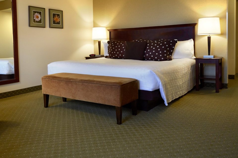 A guest room with a king bed, a dark wood headboard and an upholstered bench