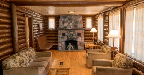 A cabin living room with a stone fireplace, a sofa and armchairs