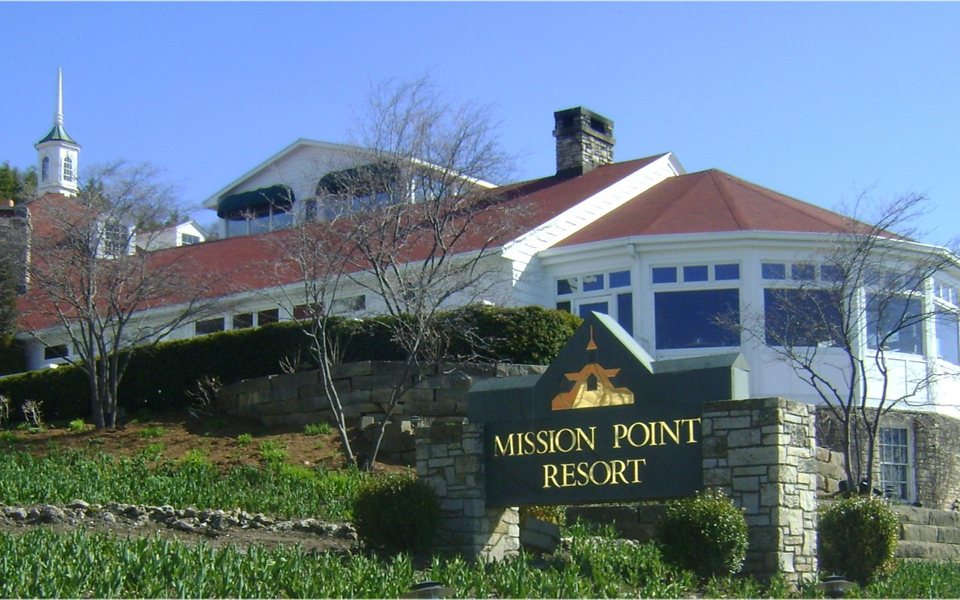 A Mission Point Resort fehér, piros tetős főépülete és a kőkeretes bejárati tábla kék ég alatt