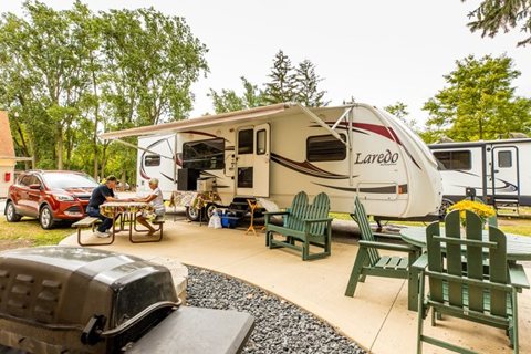 A travel trailer on a tree-shaded site with chairs