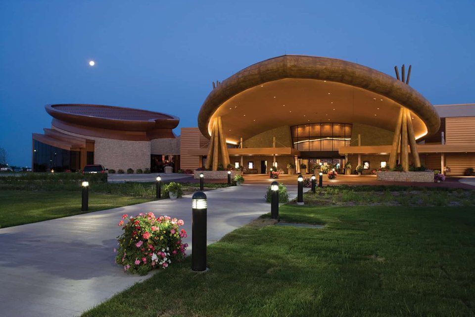 The Odawa Casino's curved-roof entrance at dusk, with a flower-lined walkway in front