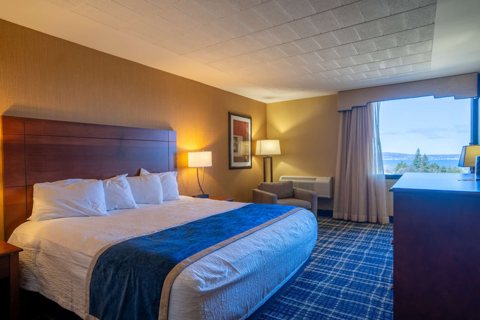 A guest room with a large bed, a blue bed runner and a window overlooking the water