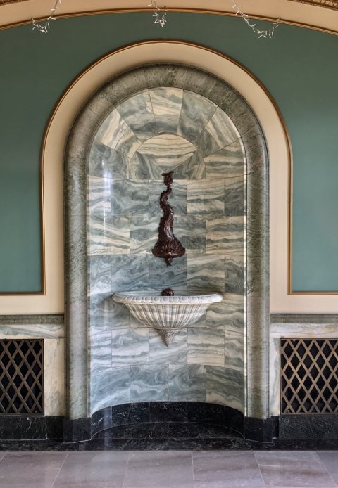 A marble-clad arched wall fountain in the building's entrance vestibule