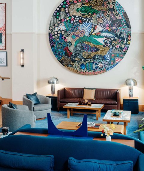 The lounge with blue sofas, a leather couch and a large round sequined artwork on the wall