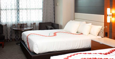 A guest room with two queen beds, a curtained window and a small round table