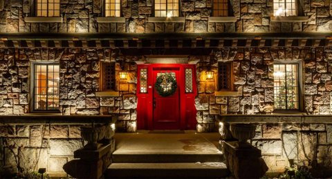 The stone house's lit red front door with a wreath
