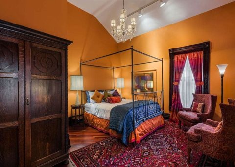 A guest room with a canopy bed, orange walls and a carved wardrobe