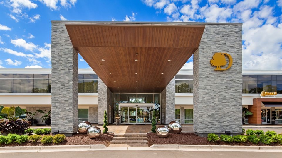 The hotel entrance with stone-clad pillars and a wood-lined canopy under a blue sky