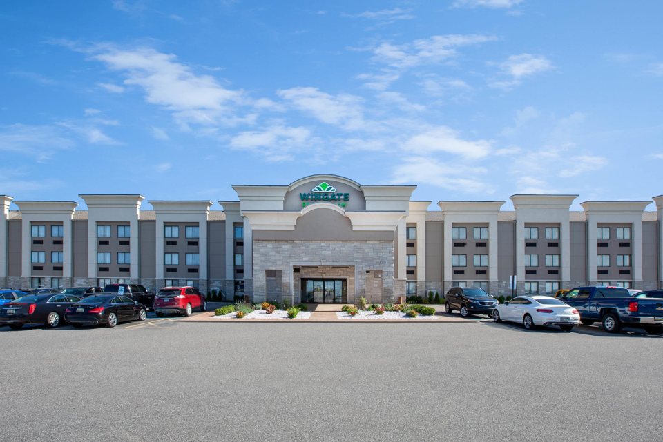 The hotel's four-storey building with its entrance and parking lot under a blue sky