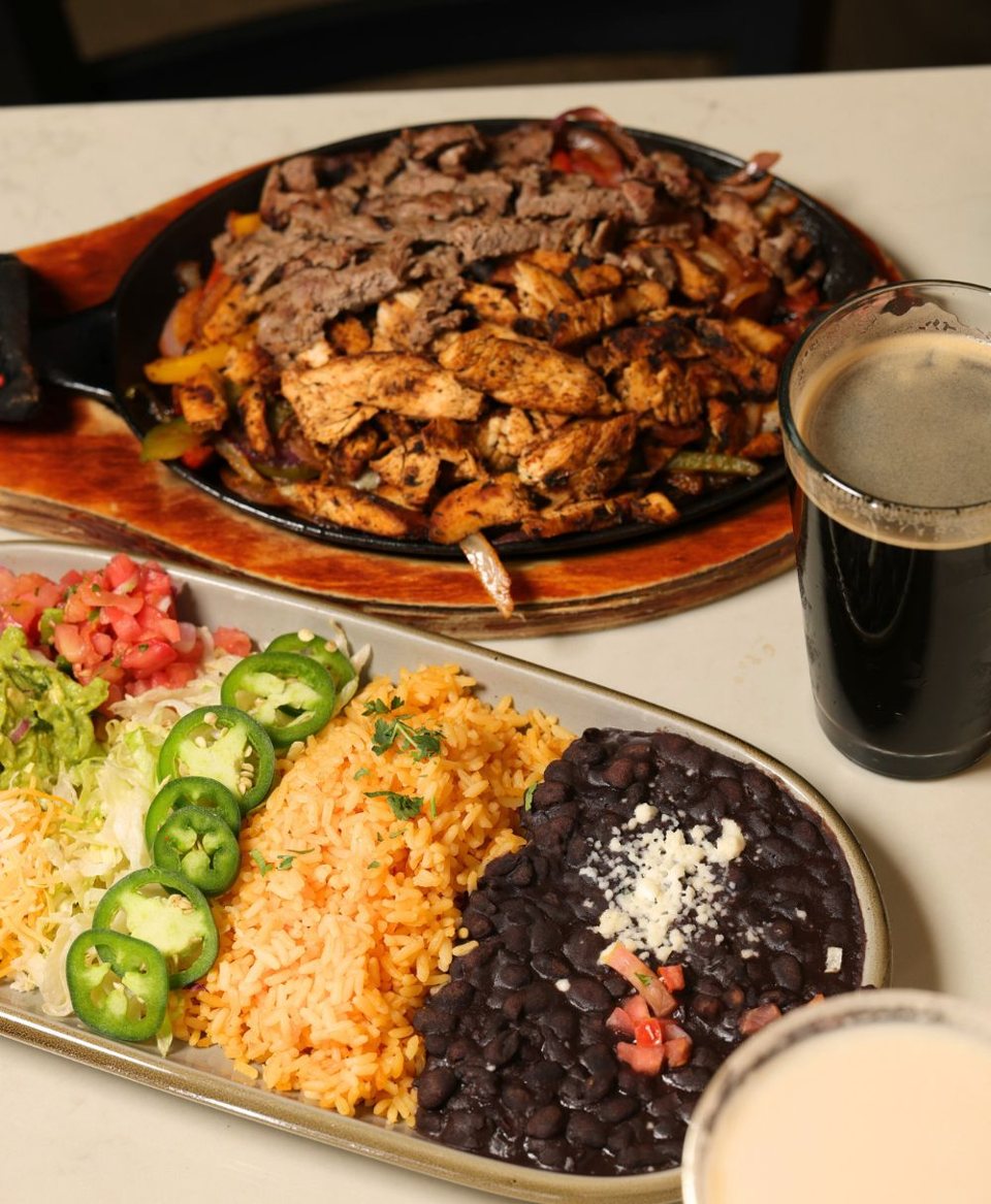 Beef and chicken fajitas in a cast-iron skillet with rice, black beans, jalapeños and a glass of dark beer