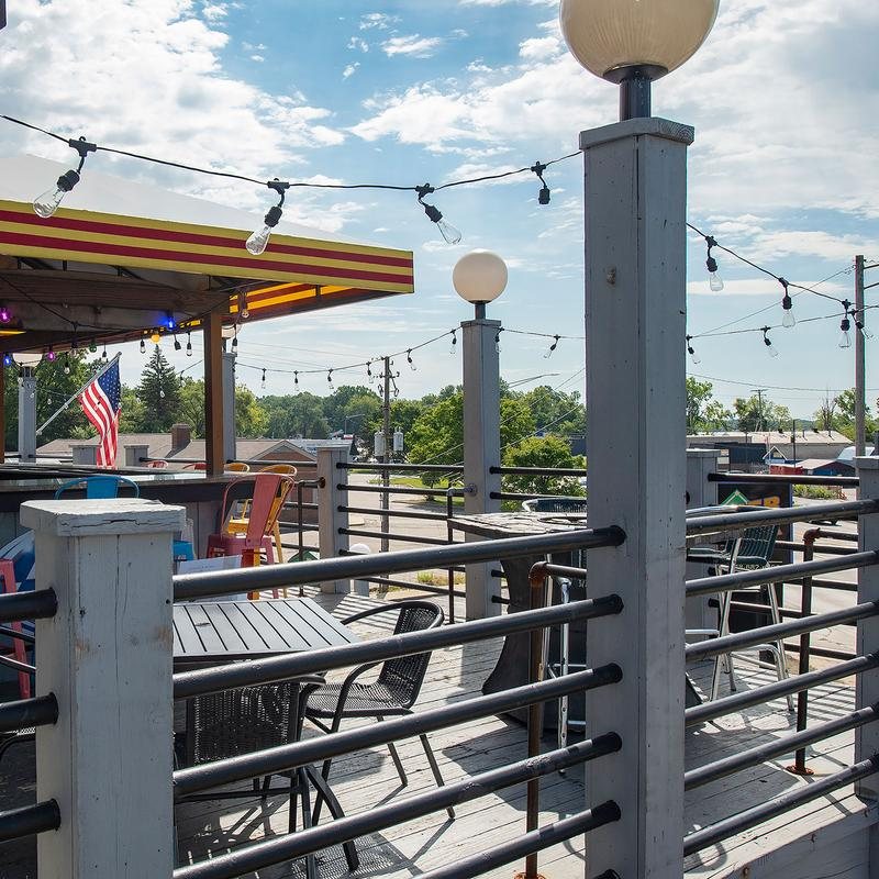 An upstairs deck with tables, string lights, colorful bar stools and an American flag