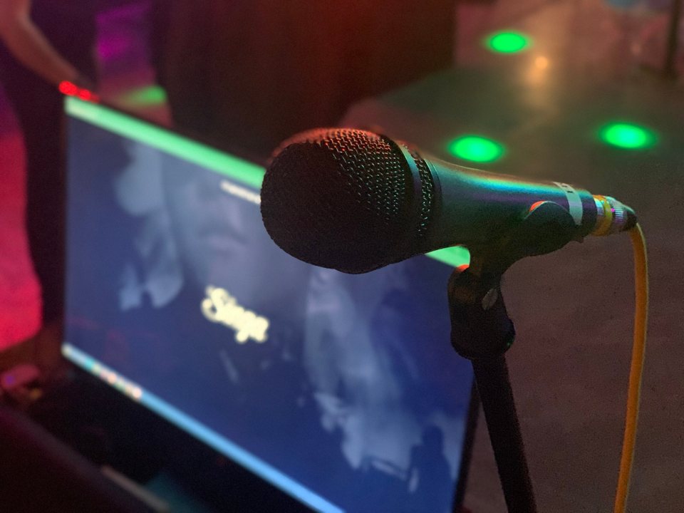 A microphone on a stand in front of a karaoke screen with green light spots